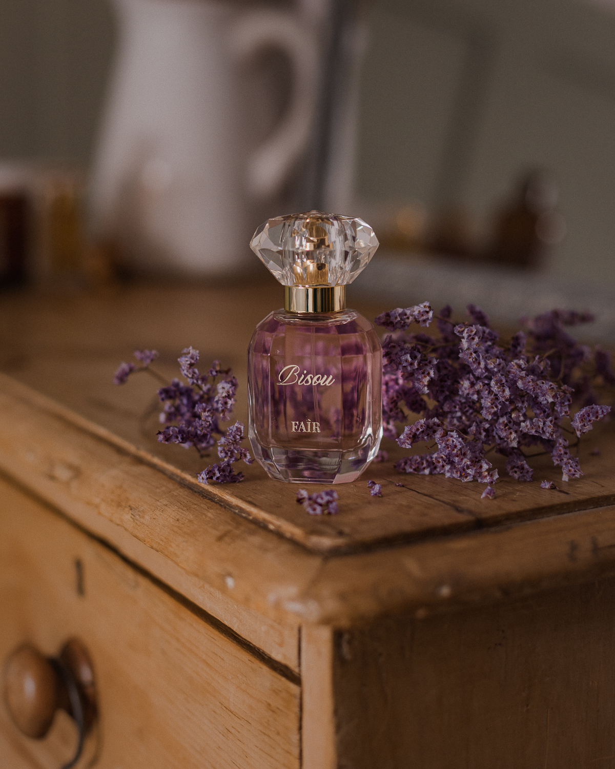 Bisou by Faîr Parfum on a dressing table surrounded by purple flowers